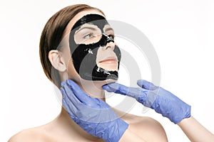 Young beautiful woman applying a mask for the face of the therapeutic black mud. Spa treatment