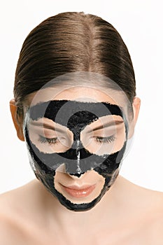 Young beautiful woman applying a mask for the face of the therapeutic black mud. Spa treatment