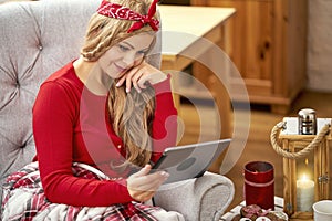 Young beautiful woman in an armchair with a tablet wrapped in a blanket during Christmas time