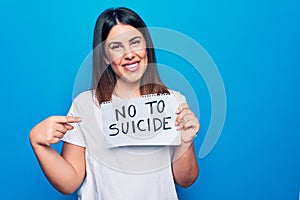 Young beautiful woman asking for psychical problem holding paper with not to suicide message smiling happy pointing with hand and
