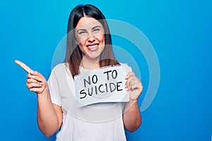 Young beautiful woman asking for psychical problem holding paper with not to suicide message smiling happy pointing with hand and