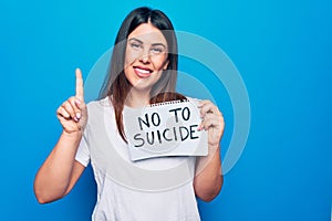 Young beautiful woman asking for psychical problem holding paper with not to suicide message smiling with an idea or question