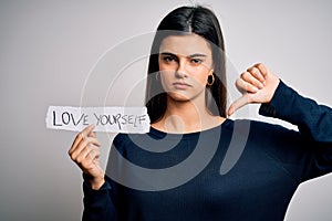 Young beautiful woman asking for take care of you holding paper with love yourself message with angry face, negative sign showing