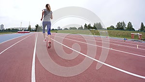 A young beautiful woman athlete in red snikers start running and runs past the camera during a day running training at