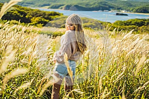 Young beautiful woman in autumn landscape with dry flowers, wheat spikes. Fashion autumn, winter. Sunny autumn, Cozy