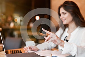 Young beautiful woman with bank card in her hand making payment using laptop while drinking hot coffee in cafe modern