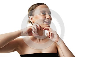 Young beautiful woman with bare shoulders doing massage to prevent double chin against white studio background.