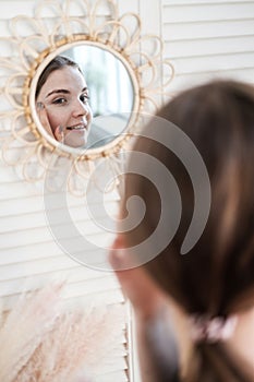 Young beautiful woman in bathroom examines her reflection in the mirror on wall. Concept of female morning skin and hair