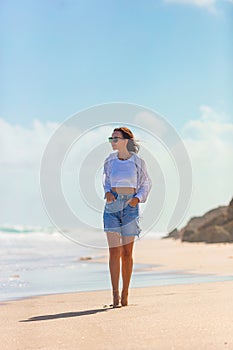 Young beautiful woman on beach vacation walking by the sea