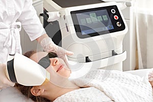 Young beautiful woman on beauty cosmetology procedure in spa salon. Therapist beautician makes a laser treatment to