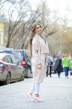 Young beautiful woman in beige coat and torn jeans and pink sneakers