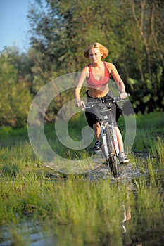 Young beautiful woman with bicycle going through water by the river