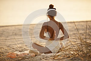 Woman in Yoga Meditation Pose with Headphones on the Beach