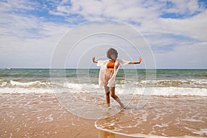 Young beautiful woman in bikini walking along the beach shore. The woman is enjoying her trip to a paradise beach while making