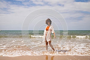Young beautiful woman in bikini walking along the beach shore. The woman is enjoying her trip to a paradise beach while making