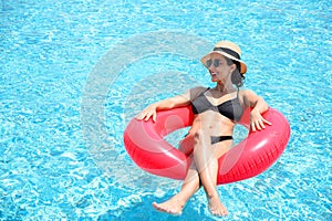 Young beautiful woman in bikini wear hat and sunglasses relaxing in swimming pool with rubber ring, Summer vacation concept