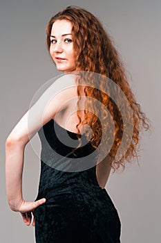 Young beautiful woman in black dress with long red hairs standing on grey background