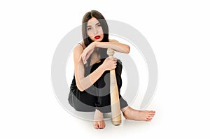 Young beautiful woman in a black dress sitting with a baseball bat on a white background