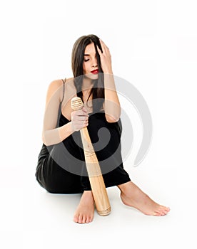 Young beautiful woman in a black dress sitting with a baseball bat on a white background