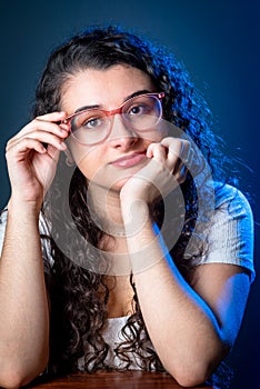 Young beautiful woman with black hair, wearing eyeglasses, with one hand on her chin