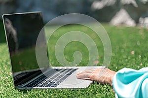 a young beautiful woman with blond curly hair in glasses and a blue dress sits on the grass in nature and uses a laptop,