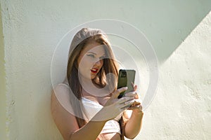 Young beautiful woman, blonde, blue eyes, leaning against a white wall checking social networks on her cell phone. Concept