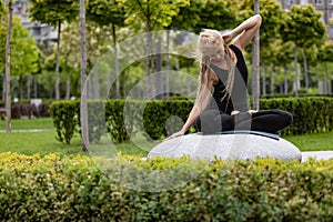 Young beautiful woman with blonde hair doing yoga exercise in green public park in summer morning, outdoors. Healthy