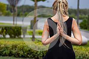 Young beautiful woman with blonde hair doing yoga exercise in green public park in summer morning, outdoors. Healthy