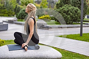 Young beautiful woman with blonde hair doing yoga exercise in green public park in summer morning, outdoors. Healthy