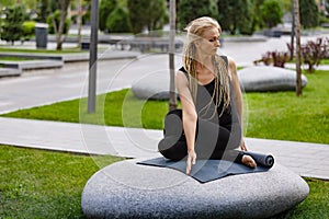 Young beautiful woman with blonde hair doing yoga exercise in green public park in summer morning, outdoors. Healthy