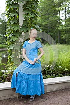 The young beautiful woman in a blue dress in the arbor twined a green bindweed