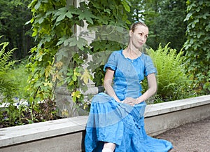 Young beautiful woman in a blue dress in the arbor twined a green bindweed