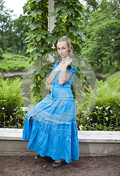 Young beautiful woman in a blue dress in the arbor twined a green bindweed