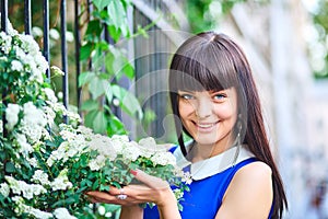 Young beautiful woman in a blue dress enjoys the smell of blooming lilacs on a sunny day. Outdoor portrait in blooming spring park