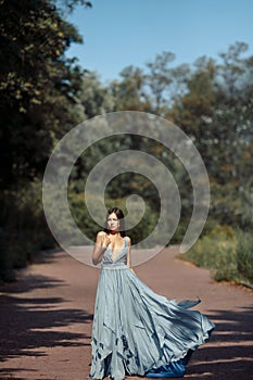 Young beautiful woman blue dress walking path in park.