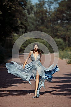 Young beautiful woman blue dress walking path in park.