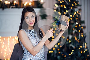 Young beautiful woman in blue elegant evening dress sitting on floor near christmas tree and presents on a new year eve