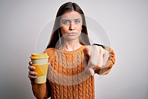 Young beautiful woman with blue eyes drinking cup of takeaway coffee over isolated background pointing with finger to the camera