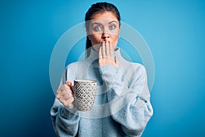 Young beautiful woman with blue eyes drinking mug of coffee over isolated background cover mouth with hand shocked with shame for