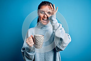 Young beautiful woman with blue eyes drinking mug of coffee over isolated background with happy face smiling doing ok sign with