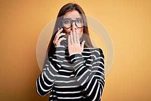 Young beautiful woman with blue eyes having conversation talking on the smartphone cover mouth with hand shocked with shame for