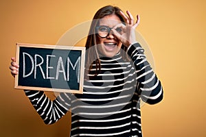 Young beautiful woman with blue eyes holding blackboard with dream message word with happy face smiling doing ok sign with hand on