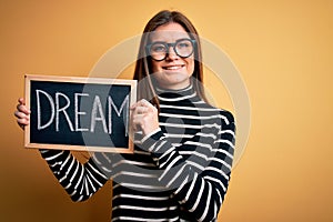 Young beautiful woman with blue eyes holding blackboard with dream message word with a happy face standing and smiling with a