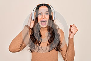 Young beautiful woman with blue eyes listening to music and dancing using headphones screaming proud and celebrating victory and