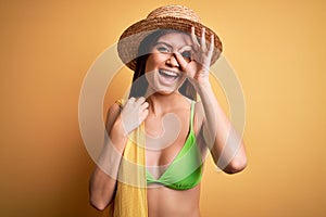 Young beautiful woman with blue eyes on vacation wearing bikini and hat holding towel with happy face smiling doing ok sign with