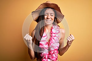 Young beautiful woman with blue eyes on vacation wearing bikini and hawaiian lei very happy and excited doing winner gesture with