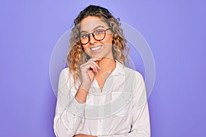 Young beautiful woman with blue eyes wearing casual shirt and glasses over purple background looking confident at the camera with