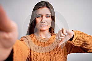 Young beautiful woman with blue eyes wearing casual sweater making selfie by camera with angry face, negative sign showing dislike