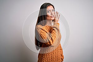 Young beautiful woman with blue eyes wearing casual sweater standing over white background hand on mouth telling secret rumor,