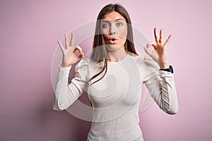 Young beautiful woman with blue eyes wearing casual white t-shirt over pink background looking surprised and shocked doing ok